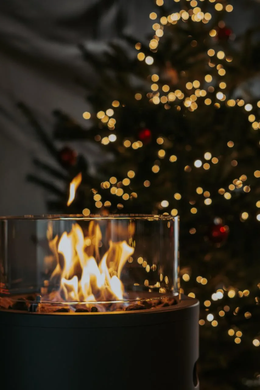 Gasfeuer in einem Glaszylinder vor einem beleuchteten Tannenbaum.