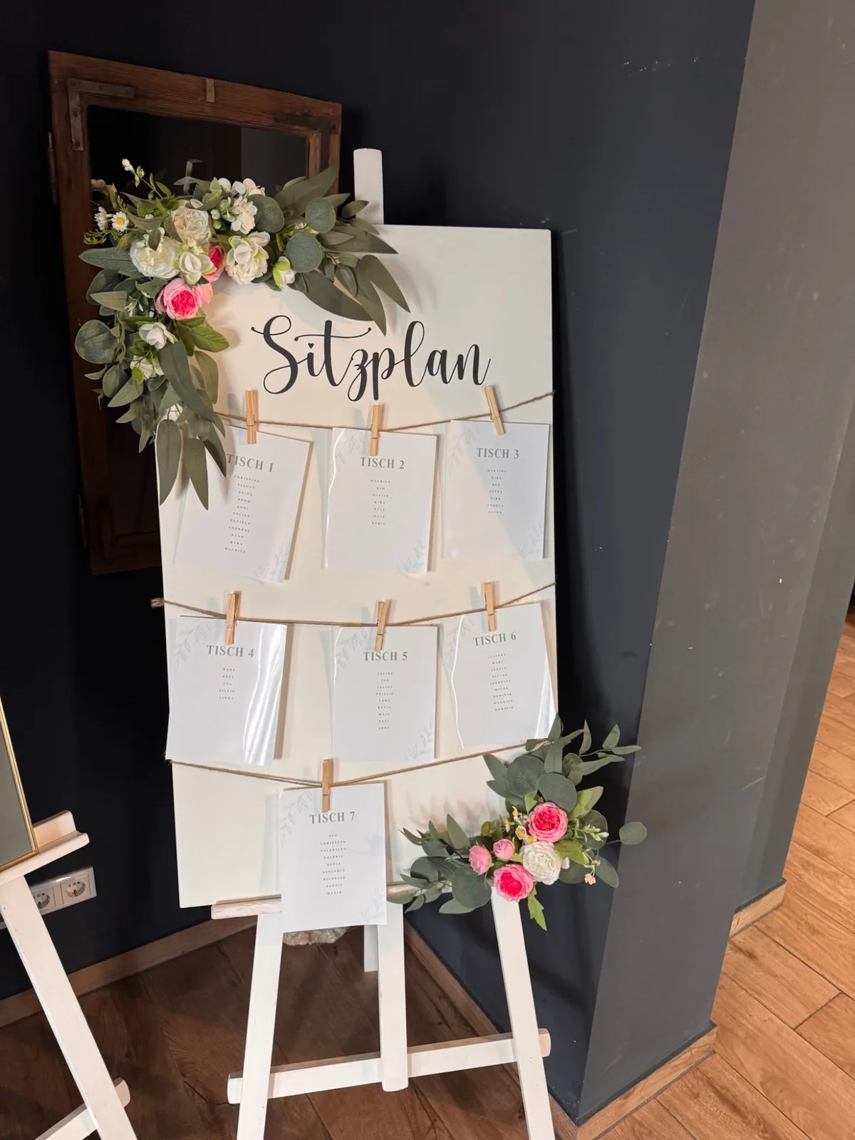 Sitzplan auf einer Staffelei, mit einem Blumengesteck geschmückt.